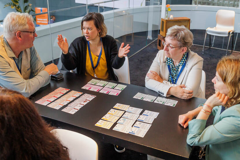 1 man en 3 vrouwen aan een tafel met een kaartspel