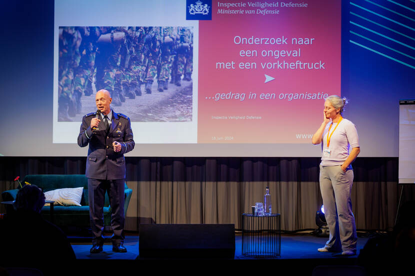 Man in uniform en vrouw op een podium voor een groot beeld