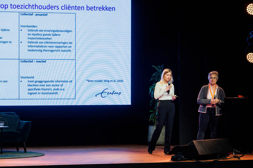 Twee vrouwen op een podium voor een groot beeldscherm